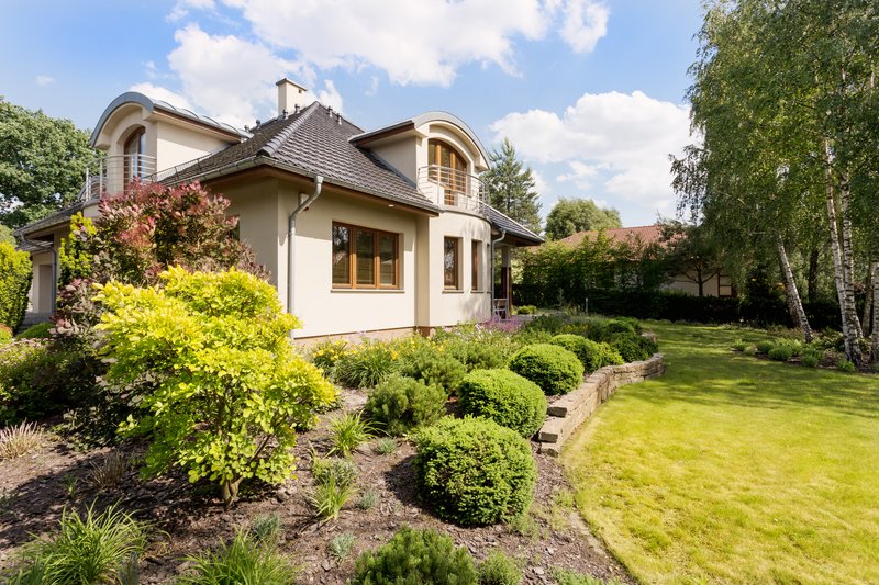 Casa rodeada de un amplio jardín verde, con arboles y arbustos pequeños