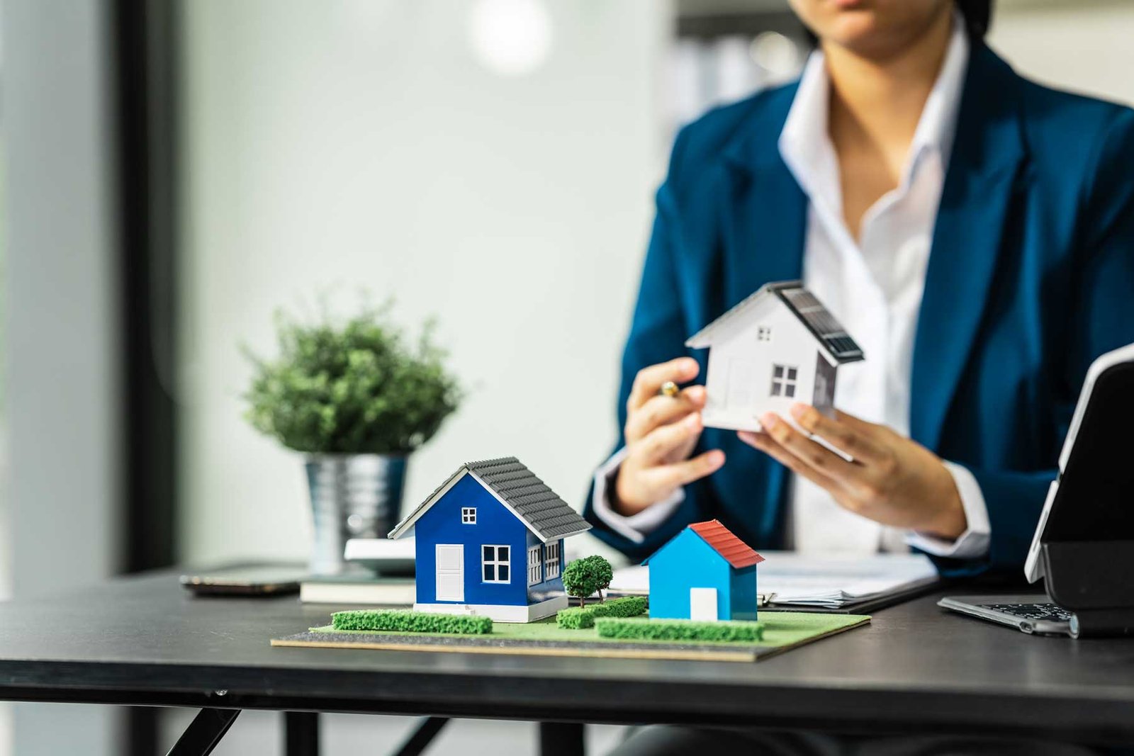 Agente de bienes raíces sentado en un escritorio, sosteniendo una casa de maqueta