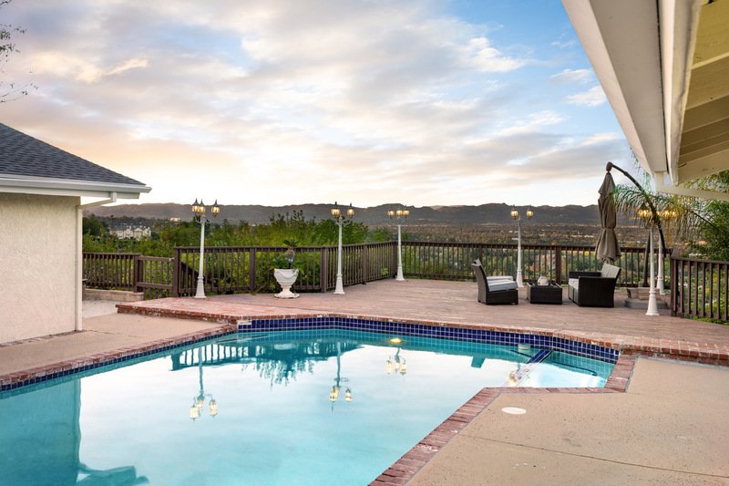 Una piscina exterior con un patio y al fondo un atardecer