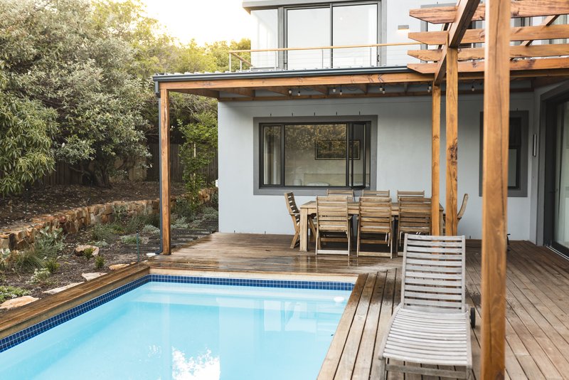 Exterior de una casa, con una alberca y una mesa de madera con un camastro para descansar